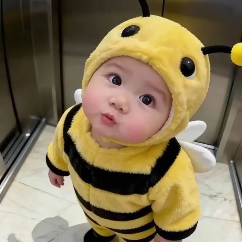 Cận cảnh em bé mặc bộ đồ ong vàng nhạt, nhìn lên với đôi mắt to tròn.