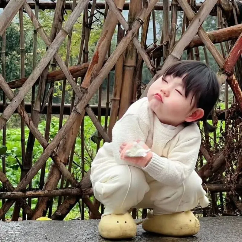 Ảnh em bé đáng yêu mặc đồ trắng đang ngồi chu mỏ, nhắm mắt hờn dỗi siêu hài hước