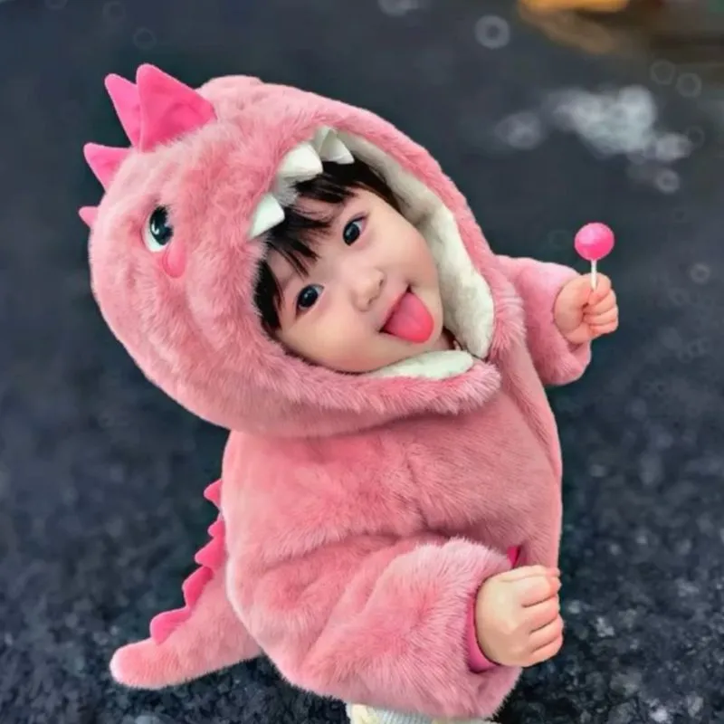 Em bé mặc bộ đồ khủng long hồng le lưỡi, tay cầm kẹo mút.