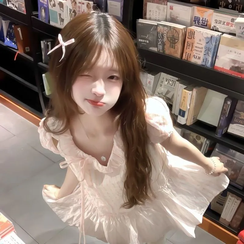 Hình ảnh avatar gái xinh k10 mặc váy hồng pastel nhẹ nhàng đang nháy mắt tinh nghịch trong hiệu sách