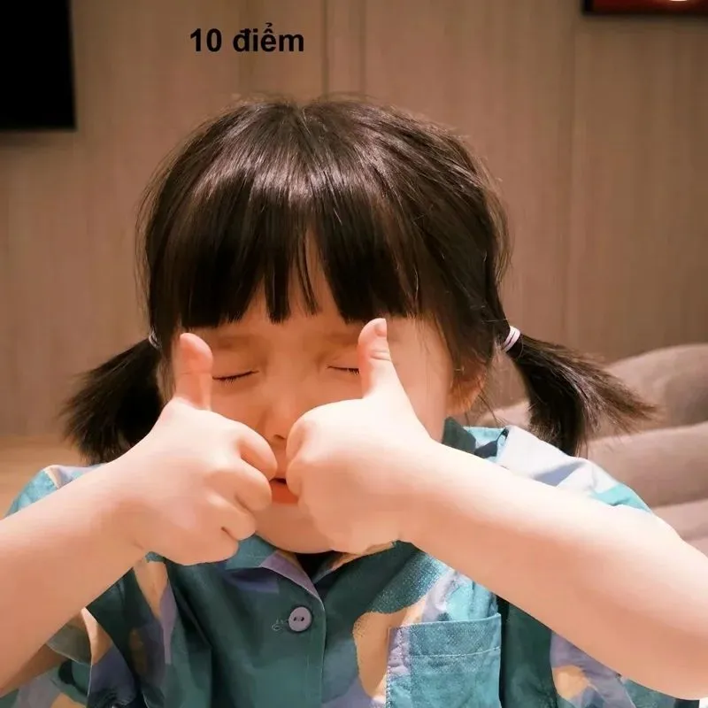 Em bé tóc hai bím mặc áo xanh đang nhắm mắt, giơ hai ngón tay cái like. Chữ "10 điểm" nhỏ ở phía trên đầu.
