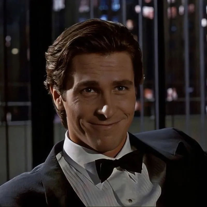 Christian Bale trong vai Patrick Bateman từ American Psycho, mặc vest đen, nụ cười nhếch mép, toan tính, trong bối cảnh tối