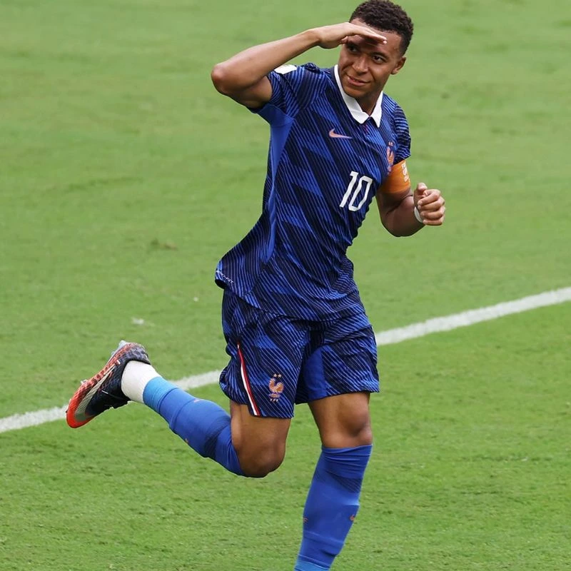 Cầu thủ Kylian Mbappe vừa chạy vừa đưa tay lên trán quan sát hướng đi của bóng