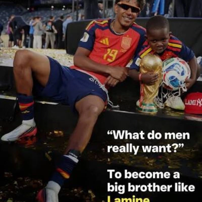 Lamine Yamal ngồi ăn mừng chiến thắng bên cạnh em bé cầm cúp và bóng World Cup