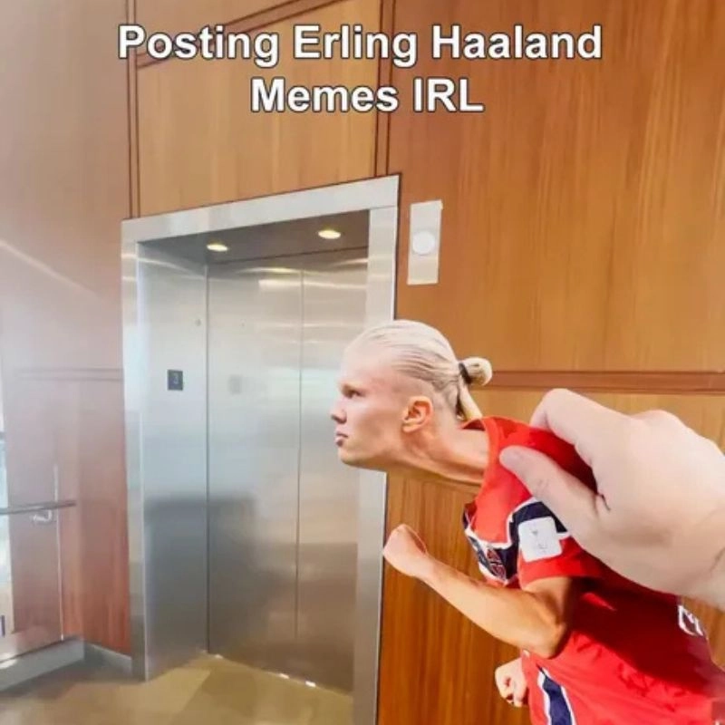 Hình ảnh bàn tay con người cầm mô hình nhân vật Haaland đang tạo dáng hài hước trước thang máy