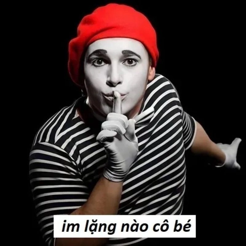 Kịch sĩ mặt trắng đội mũ nồi đỏ đưa ngón tay lên môi ra hiệu giữ trật tự